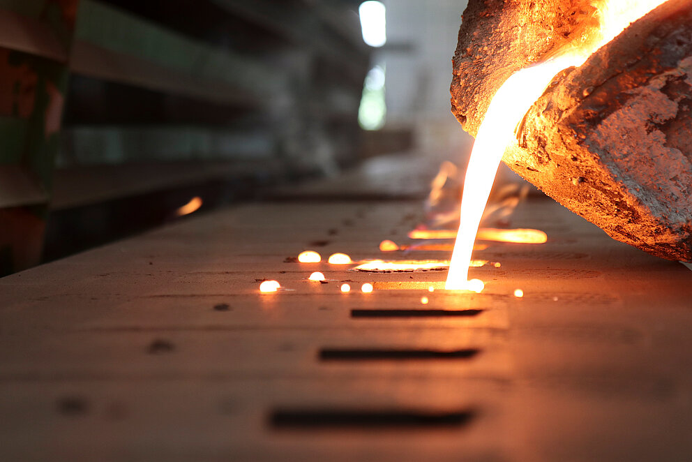 Es ist eine Nahaufnahme in einem Stahlwerk zu sehen. Dabei wird flüssiger, heißer Stahl in eine Form gegossen.