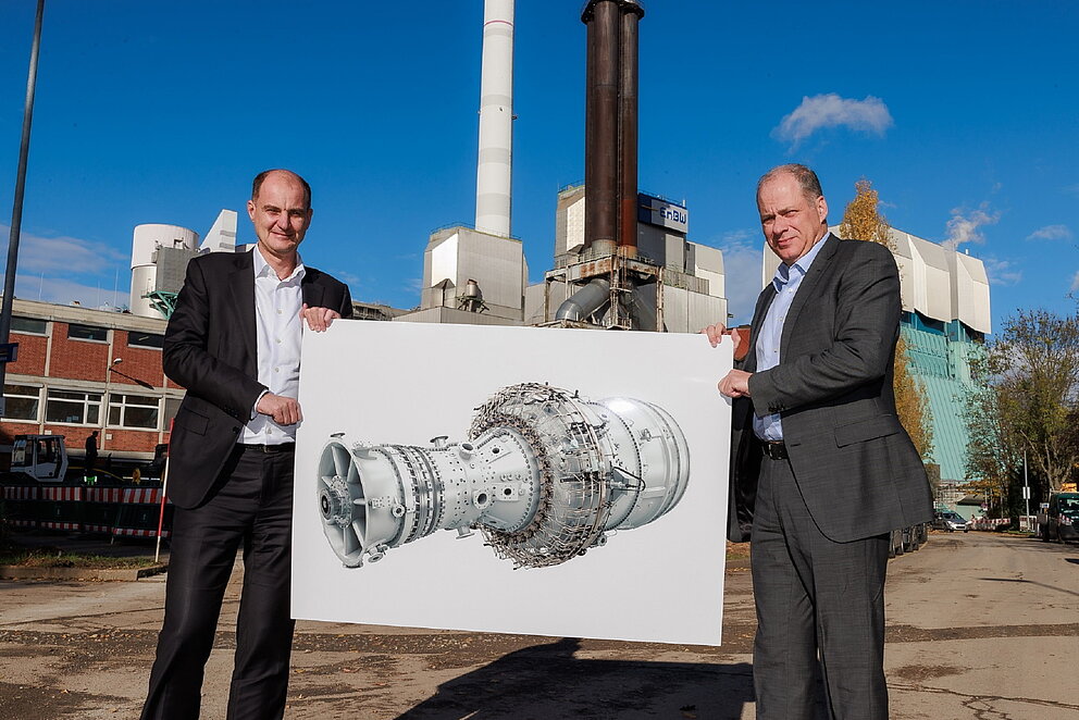Die Vorstände von EnBW und Siemens Energy Vorstand halten eine Abbildung der neuen Turbinen in der Hand