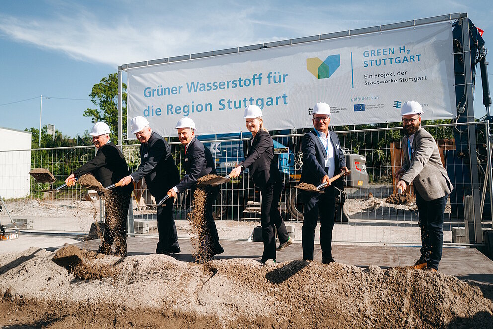 Sechs Personen mit weißem Helm und Schaufeln in der Hand posieren für ein Foto auf einer Baustelle des Projekts.