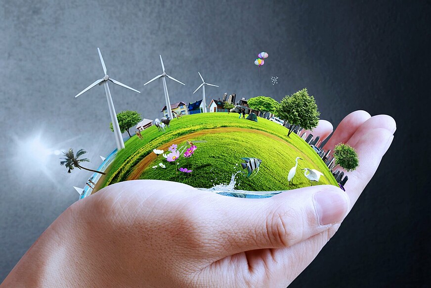 Weltkugel bedeckt mit grünem Gras, Bäumen und Windrädern wird in einer Hand gehalten.