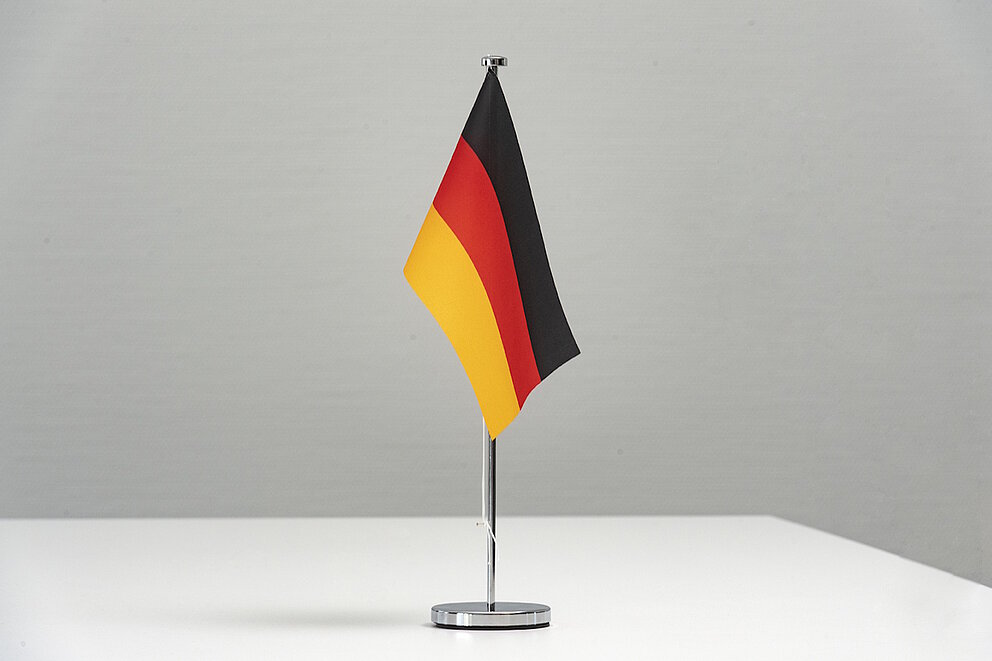 Vor schlichtem Hintergrund steht eine Deutschlandfahne.