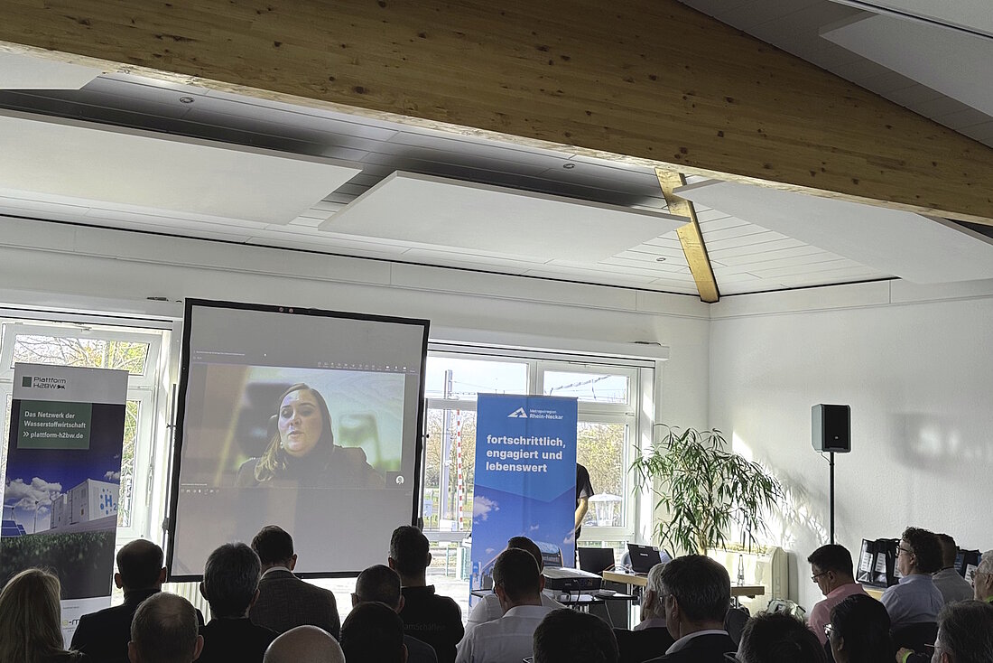 Eine Person spricht per Videokonferenz zugeschalten zum Publikum.