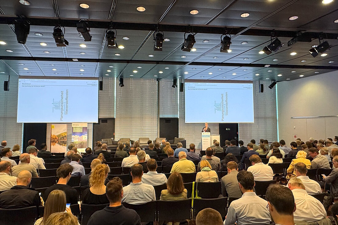 Rund 300 Personen sitzen in Saal und blicken nach Vorne zur Moderatorin.