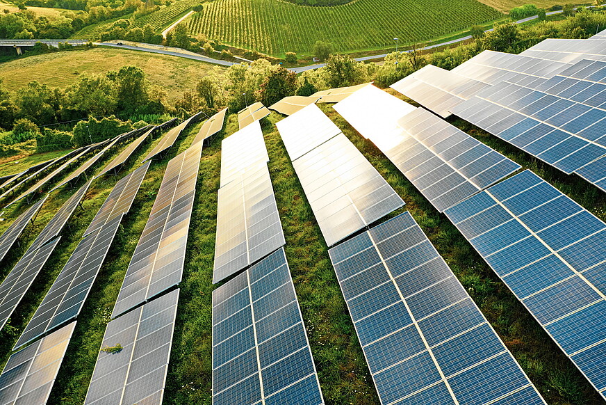 Photovoltaikanlage auf grüner hügeliger Landschaft wird von Sonne beschienen.