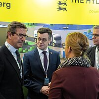 Vor dem gelben Messestand der e-mobil BW sind Vertreterinnen und Vertreter aus Baden-Württemberg mit dem andalusischen Minister im Gespräch.