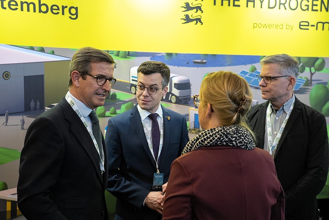 Vor dem gelben Messestand der e-mobil BW sind Vertreterinnen und Vertreter aus Baden-Württemberg mit dem andalusischen Minister im Gespräch.
