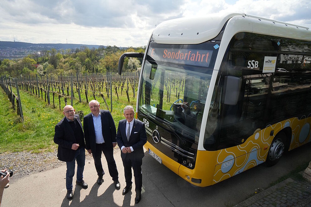 Drei Männer stehen in den Weinbergen vor einem Bus.