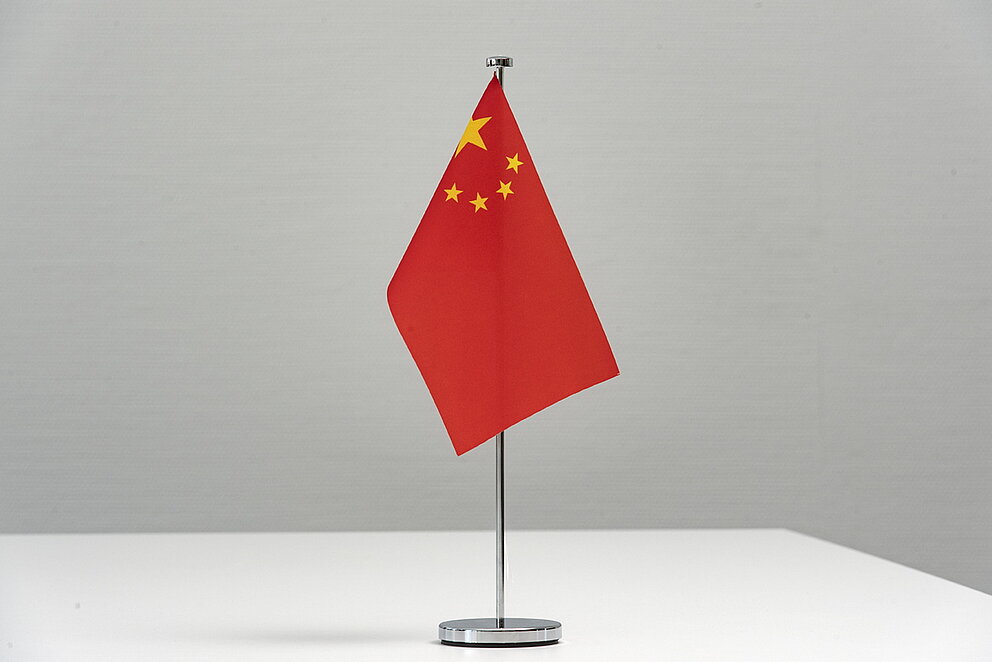 Die rote Flagge Chinas steht an einer Halterung hängen vor weißem Hintergrund.