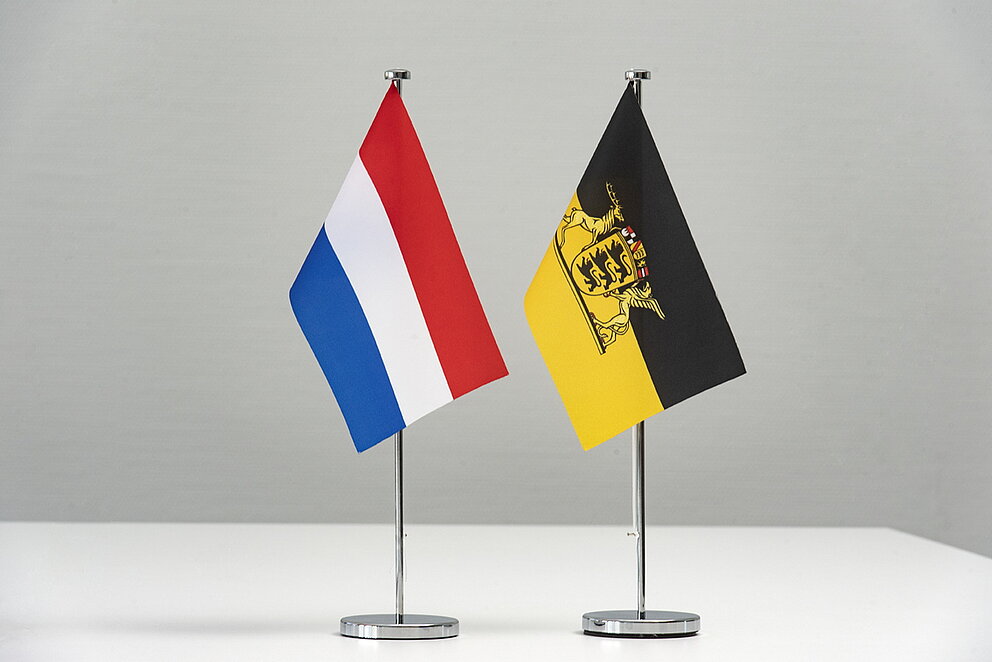 Die beiden Flaggen der Niederlande und Baden-Württembergs stehen nebeneinander vor neutralem Hintergrund.