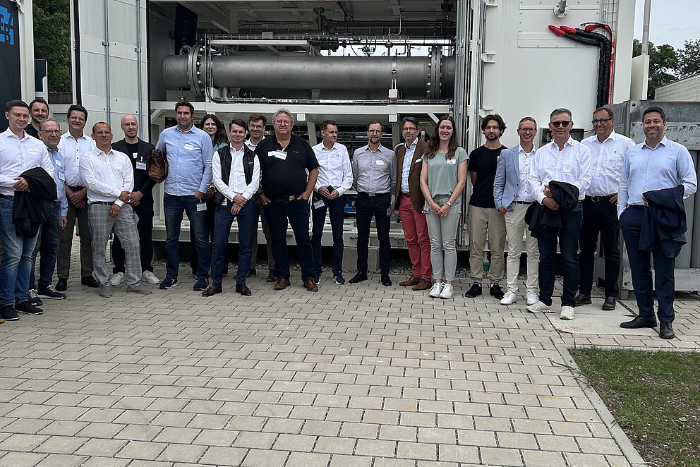 Vor einem großen Container mit einer Gasflasche stehen rund 20 Personen und posieren für ein Gruppenfoto.