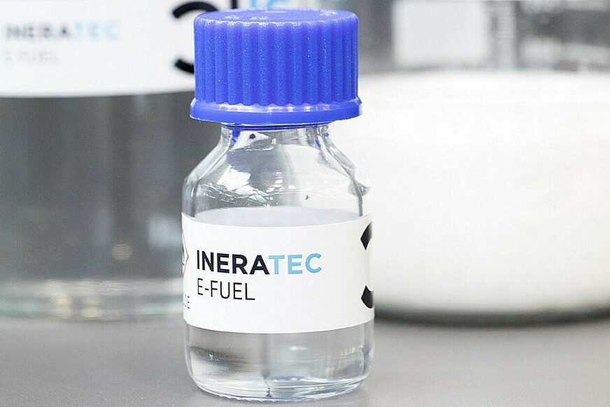 Eine Glasflasche mit durchsichtiger Flüssigkeit und der Aufschrift "e-Fuel" steht auf einem Labortisch.