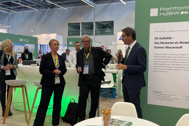Staatssekretär Dr. Andre Baumann besucht beim offiziellen Messenrundgang der Ausstellung der f-cell den Stand der Plattform H2BW und hält eine Rede vor Publikum.