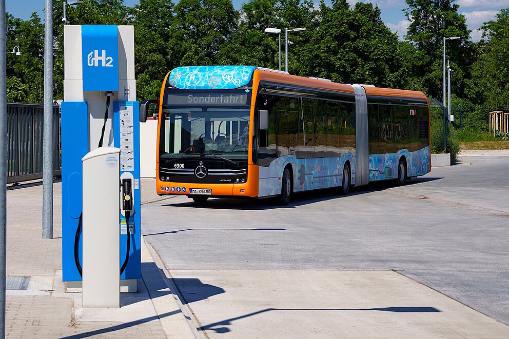 Ein Gelenkbus mit Brennstoffzellenantrieb fährt an eine Wasserstofftankstelle.