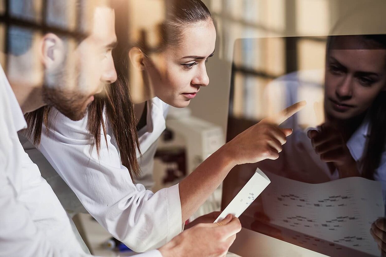Zwei Kolleg:innen arbeiten gemeinsam an einem Computer-Bildschirm
