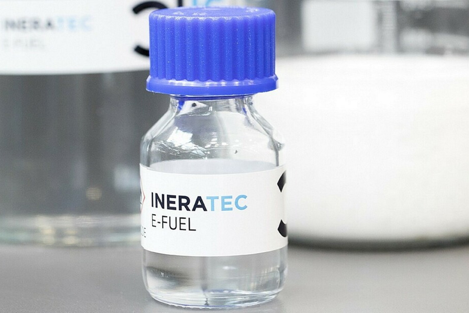 Eine Glasflasche mit durchsichtiger Flüssigkeit und der Aufschrift "e-Fuel" steht auf einem Labortisch.