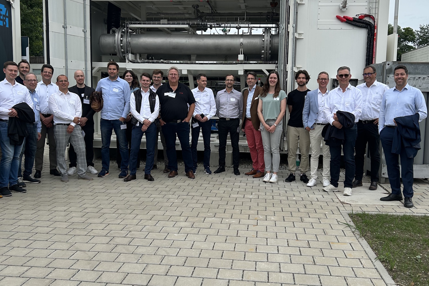 Vor einem großen Container mit einer Gasflasche stehen rund 20 Personen und posieren für ein Gruppenfoto.