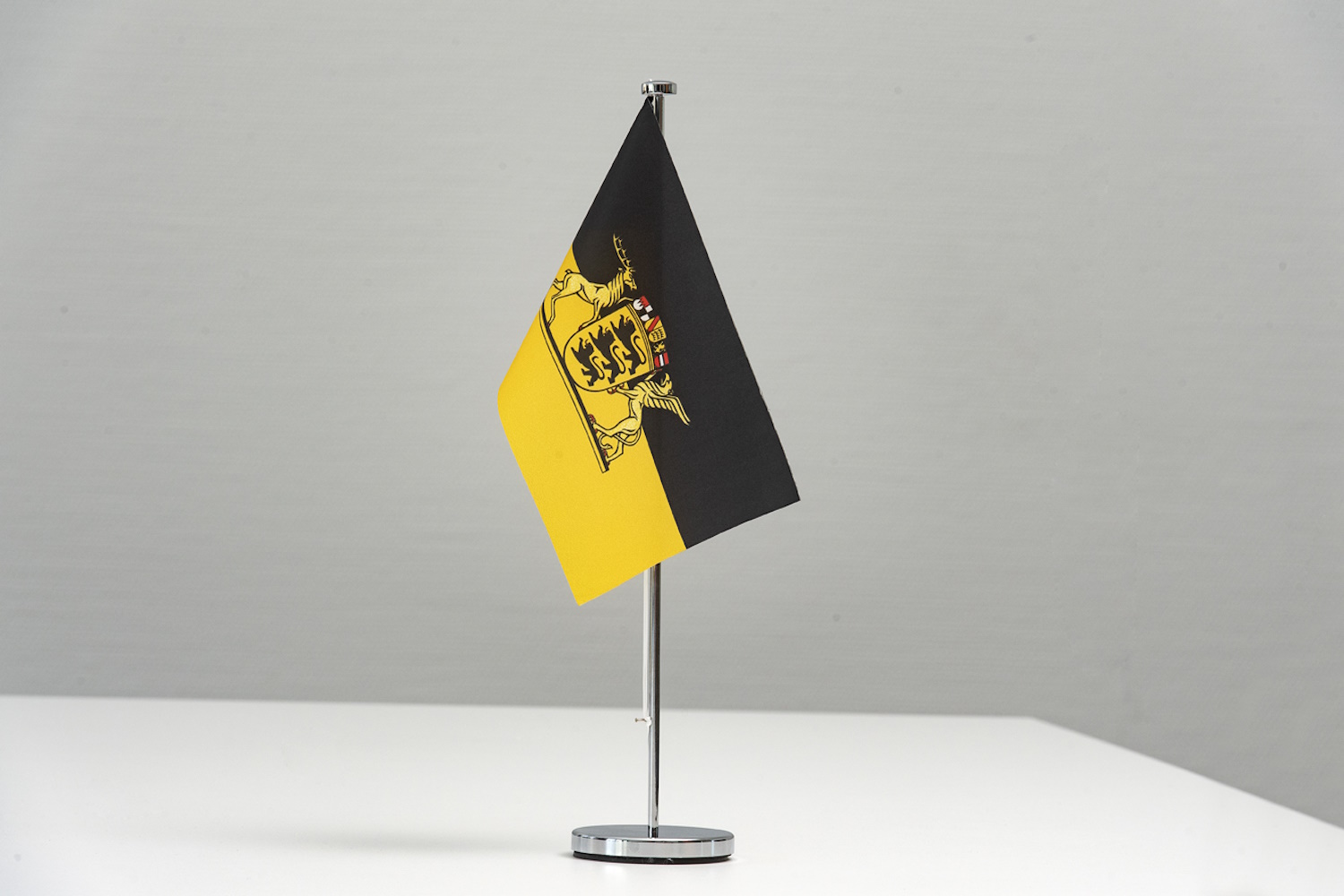 Kleine Flagge des Landes Baden-Württemberg ist an Ständer befestigt und steht vor weißem Hintergrund.