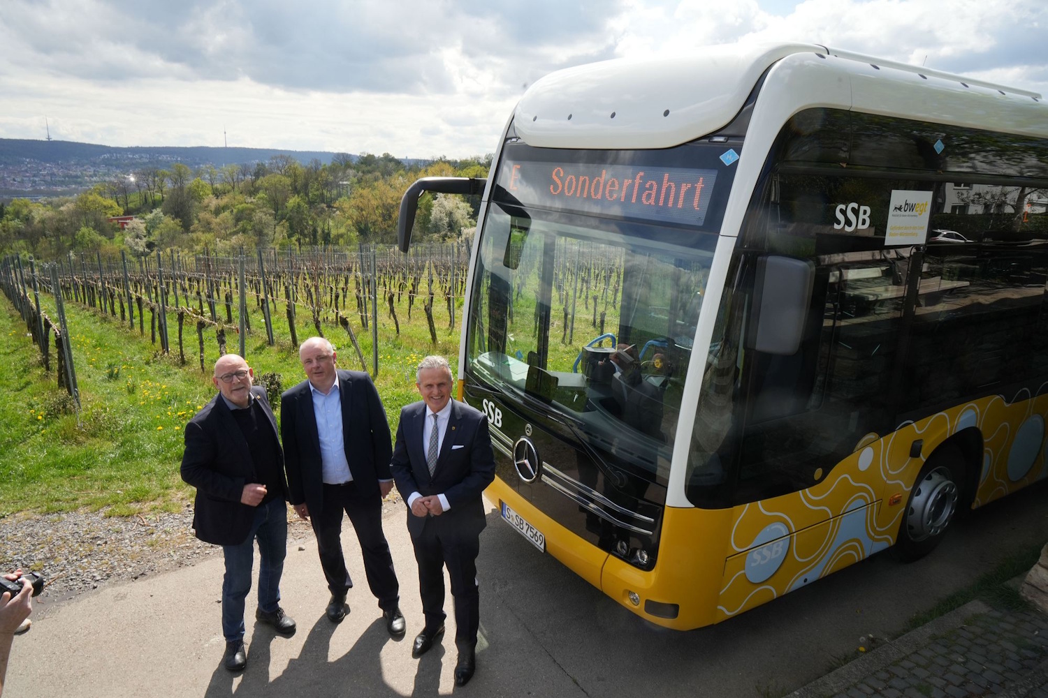 Drei Männer stehen in den Weinbergen vor einem Bus.