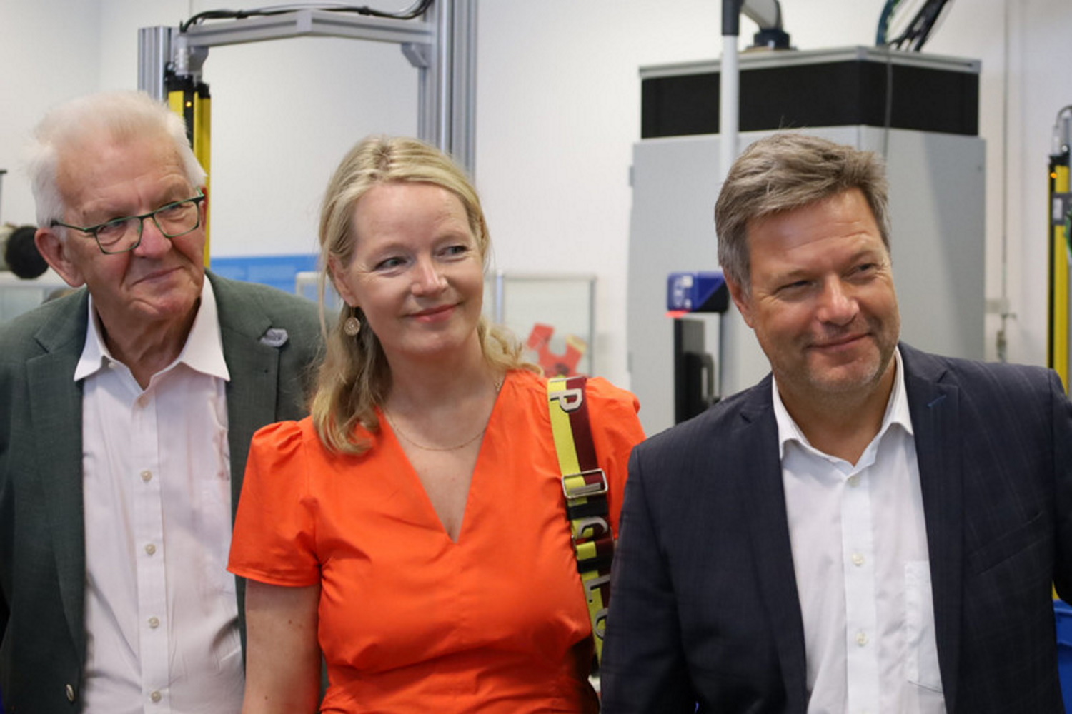 Winfried Kretschmann, Thekla Walker und Robert Habeck stehen in der Produktionshalle bei Bosch und lächeln in die Kamera.