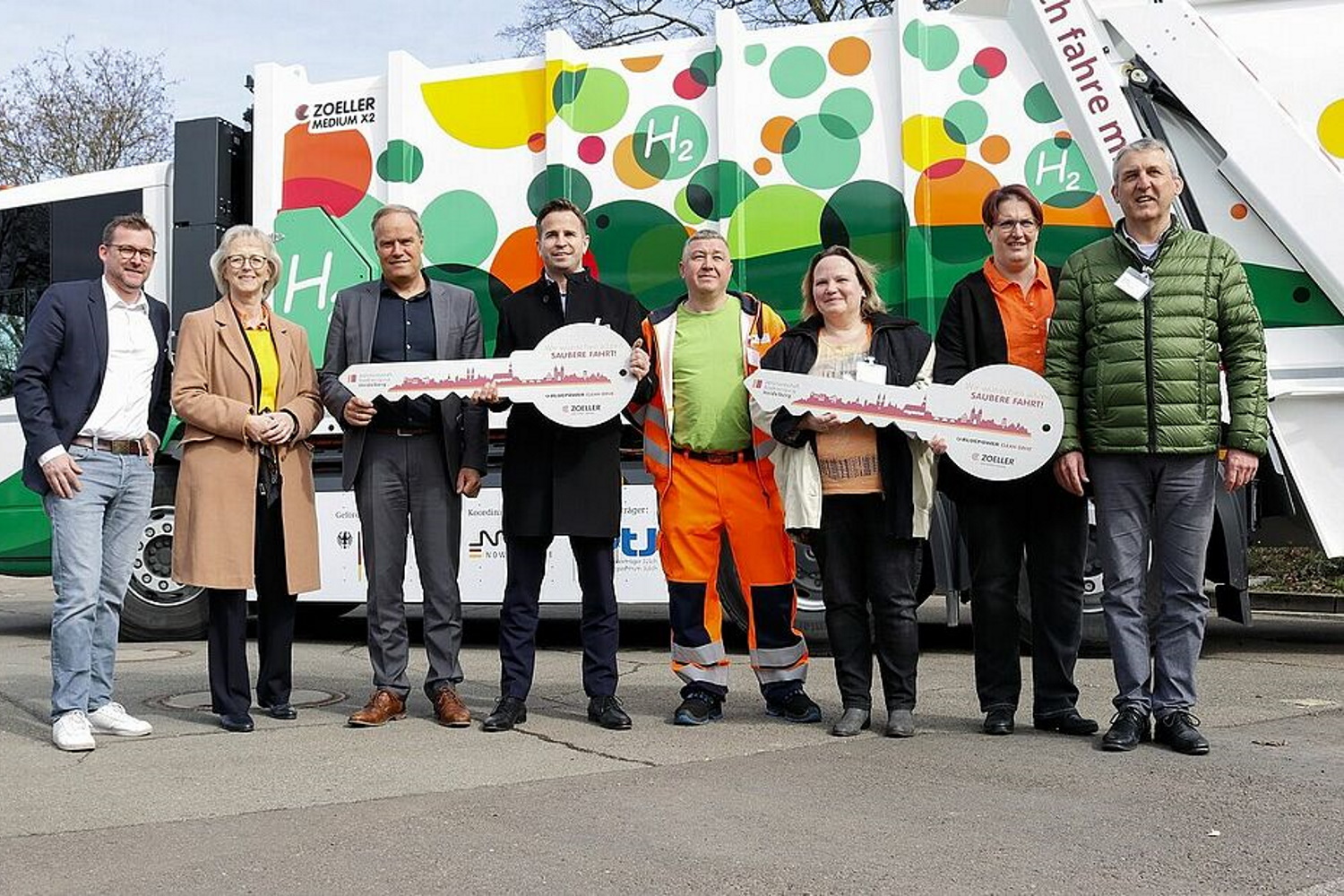 Oberbürgermeister der Stadt Heidelberg Dr. Eckert Würzner steht mit Repräsentanetn der Projektpartner vor dem Wasserstofffahrzeug der Müllabfuhr und hält einen symbolischen großen Schlüssel in den Händen