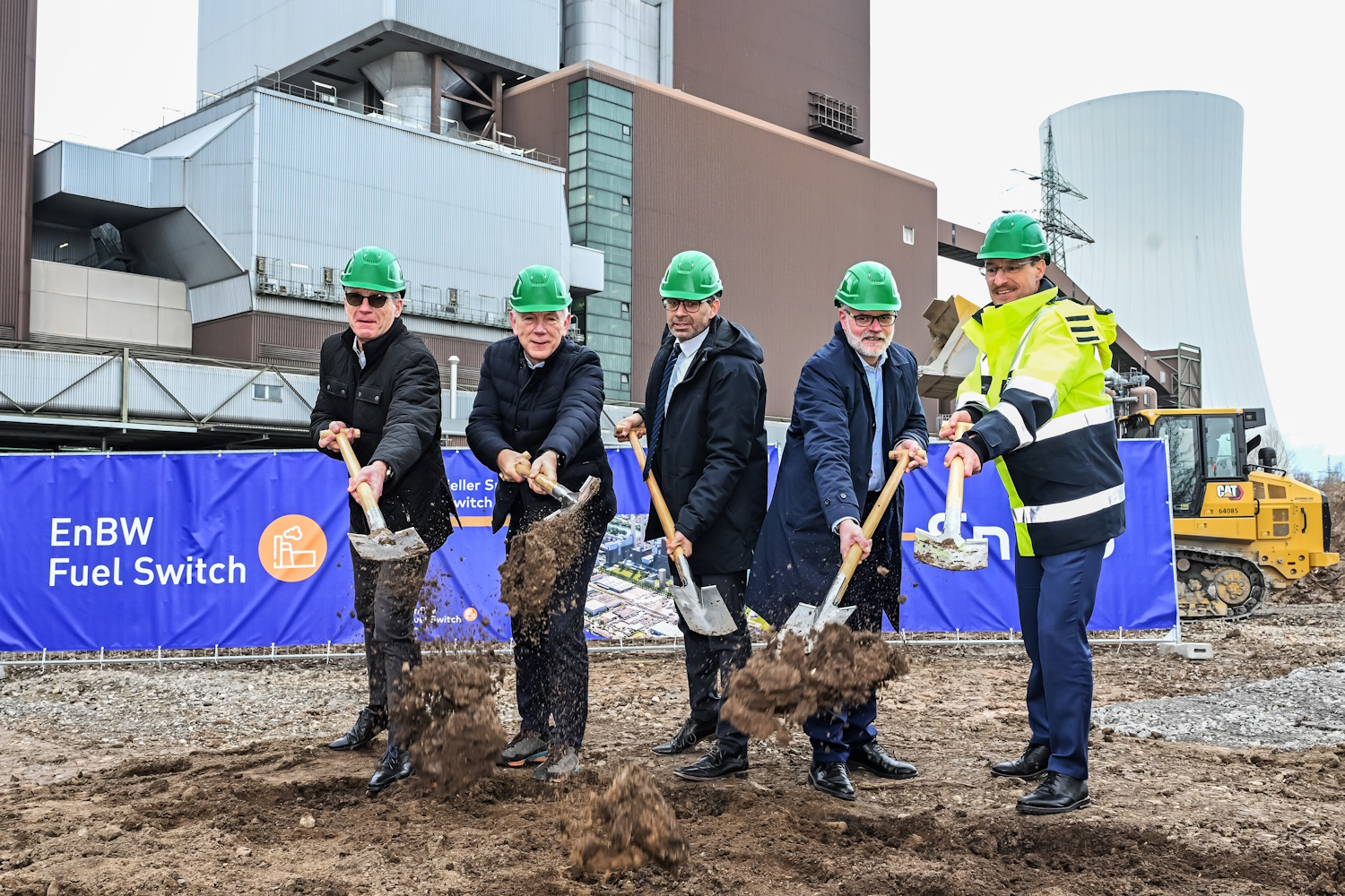 Fünf Personen, darunter der Staatssekretär des baden-württembergischen Umweltministeriums und EnBW-Vorstand Dirk Güsewell, stehen auf einer Baustelle und werfen mit Spaten etwas Erde in die Luft (sie schaufeln).