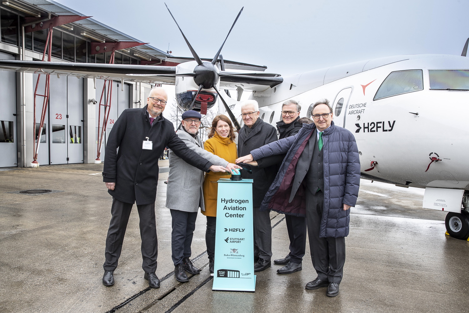 Gruppe von Personen stehen vor Flugzeug auf Flughafengelände Stuttgart und recken die Hände gemeinsam in die Mitte.