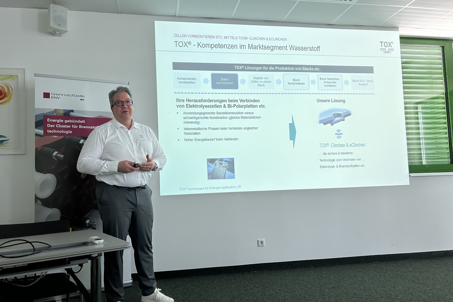 Ein Mann steht vor einer Leinwand und präsentiert Technologien in einem Vortrag.