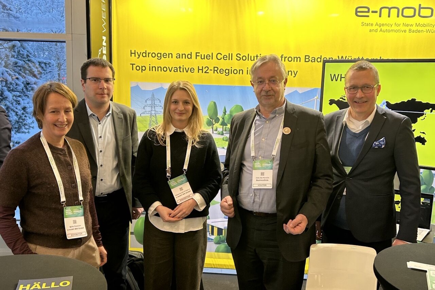 Fünf Personen stehen vor einer gelben Messewand mit Logo der e-mobil BW und lächeln in die Kamera.